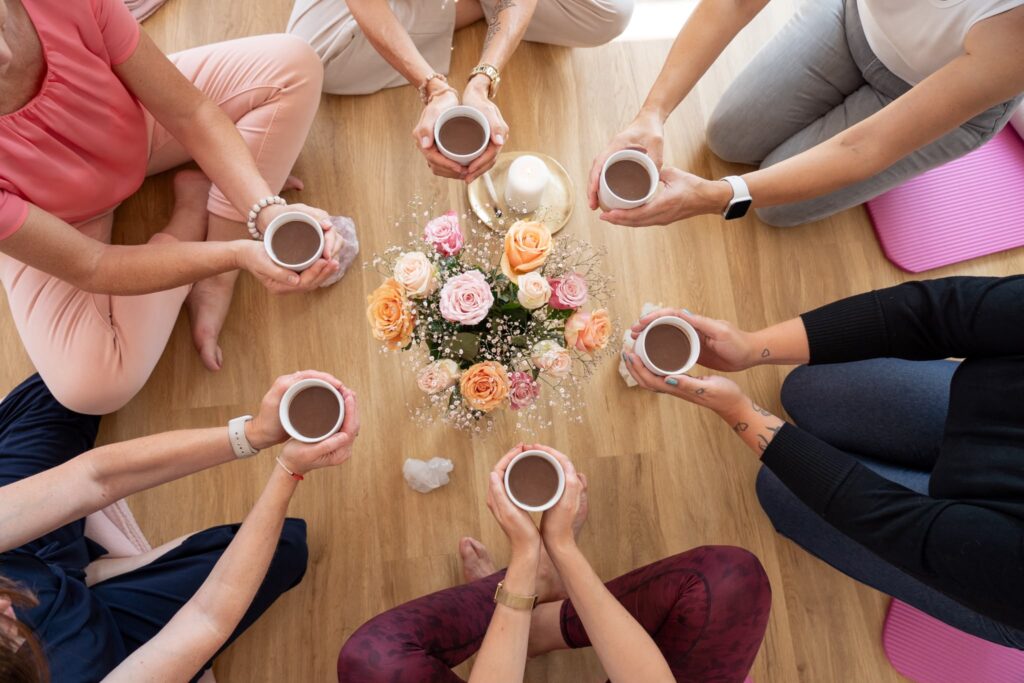 Frauen sitzen in einer achtsamen Runde mit warmen Getränken und Blumen